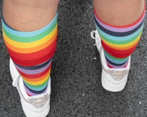 Close up rear view of legs and feet of person wearing knee high socks with colorful repeating rainbow rings design and white athletic shoes and who...