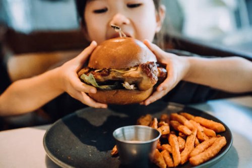 close up shot of lovely little asian girl enjoying eating a big burger with sweet potato fries in a restaurant. eating out lifestyle - junk food stock pictures, royalty-free photos & images