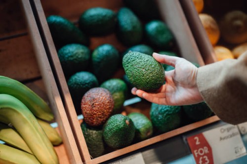 close up shot of woman’s hand holding avocado in grocery store - food stock pictures, royalty-free photos & images