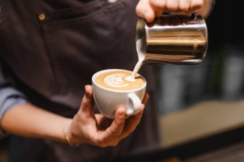 close up view of young woman preparing a coffee by drawing a flower with milk - coffee stock pictures, royalty-free photos & images