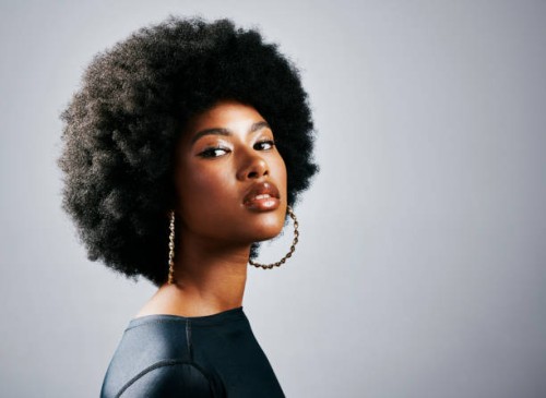 closeup of a young, stylish, and edgy black woman standing or posing against a grey studio background alone. one confident, trendy and sassy female with an afro looking powerful and wearing makeup - fashion stock pictures, ro