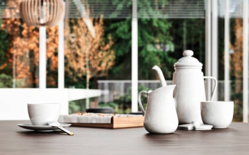 closeup of breakfast or afternoon tea: a white porcelain cup of hot tea/coffee, a mug of milk, a tray of pastries, and a teapot on a hardwood table with a green and brown autumn garden view - garden decoration stock pictures