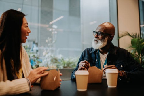 co-workers sit in a cafeteria and have a discussion as they enjoy some take out food and hot drinks - junk food stock pictures, royalty-free photos & images