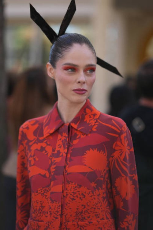 Coco Rocha wears a large hair bow tie, a red and orange floral print jacket, flared pants, outside Akris, during the Womenswear Spring/Summer 2024 as...