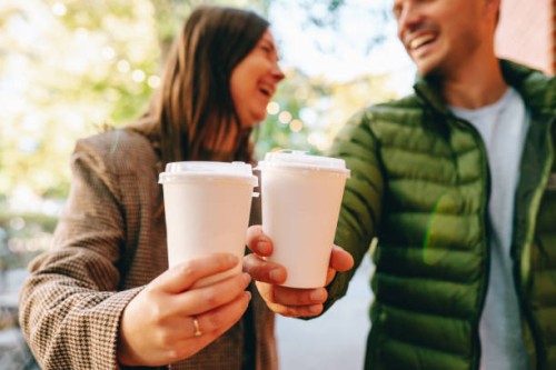 coffee on go during date: woman and man laugh while sipping coffee from biodegradable cups - junk food stock pictures, royalty-free photos & images