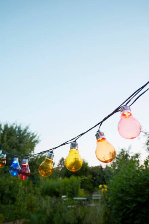 colorful string lights for party decoration in garden against sky - garden decoration stockfoto's en -beelden