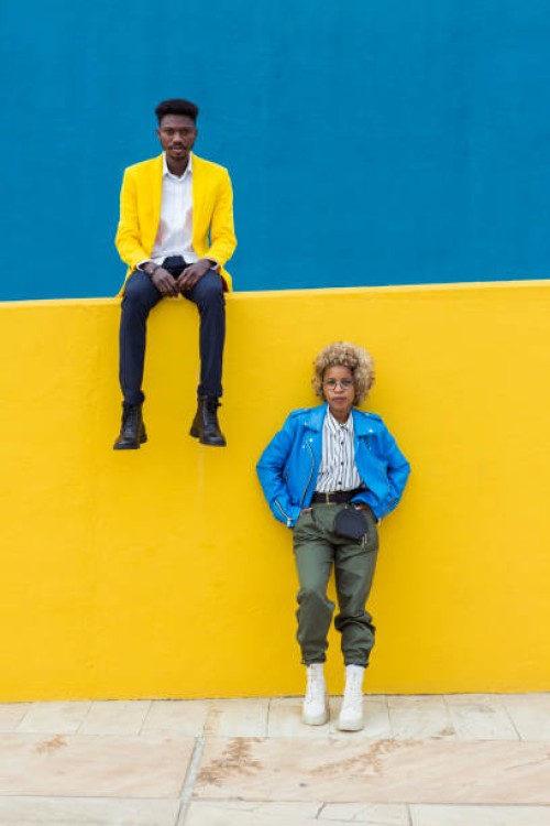 confidence portrait of two young black friends standing against a yellow wall. young trendy african man and latin american woman looking at camera outdoors. friendship and diversity concept. - fashion stock pictures, royalty-