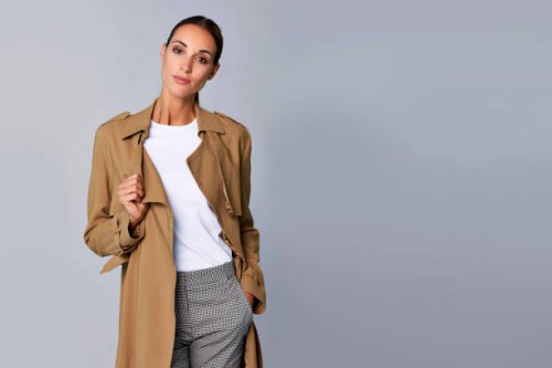 confident young woman holding brown trench coat - fashion stock pictures, royalty-free photos & images