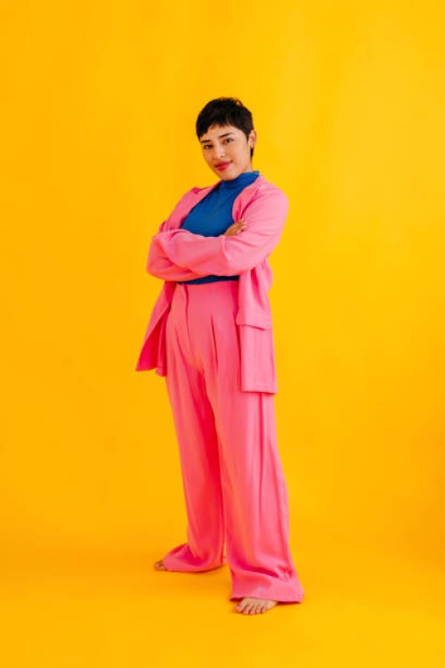 confident young woman standing with arms raised over yellow background - fashion stock pictures, royalty-free photos & images
