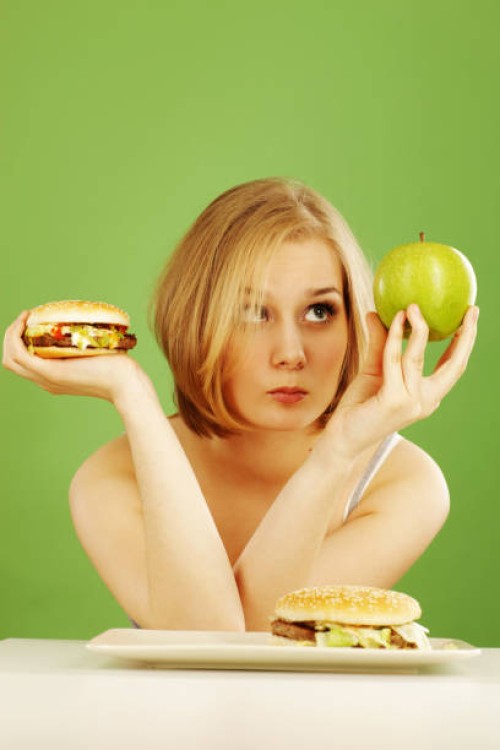 contemplative woman holding apple and hamburger deciding - junk food stock pictures, royalty-free photos & images