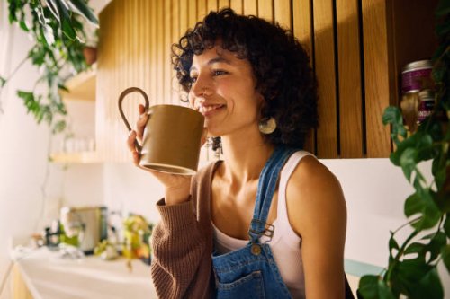 content woman savoring the aroma of her morning coffee in a well-lit kitchen with modern wooden accents and lush houseplants, embracing a moment of serenity, symbolizing mindfulness and the joy of simple pleasures in everyday