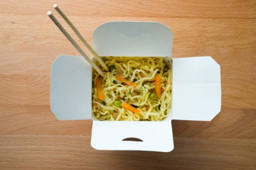 cooked instant noodles, sprinkled with spices, vegetables and herbs, freeze-dried meat. nearby are wooden chopsticks. asian chicken soup with ramen noodles in a paper box, on the dining room kitchen table. the concept of home