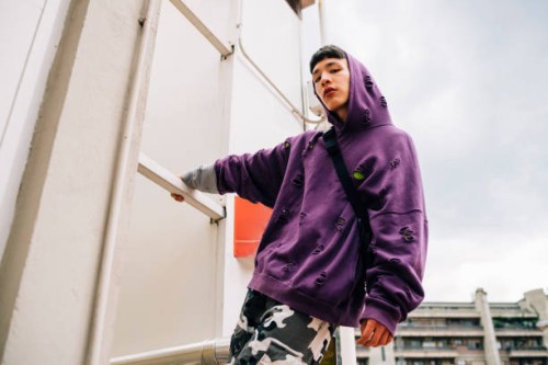 cool young man wearing hooded shirt standing on metallic ladder against sky - fashion stock pictures, royalty-free photos & images