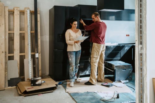 couple discussing over document while fixing cabinet together in kitchen during home renovation - home decoration stock pictures, royalty-free photos & images