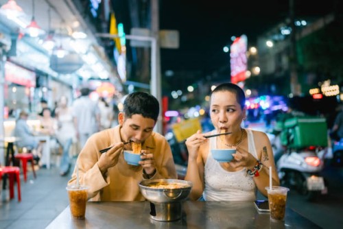 couple enjoying hot noodles at night street market - food stockfoto's en -beelden