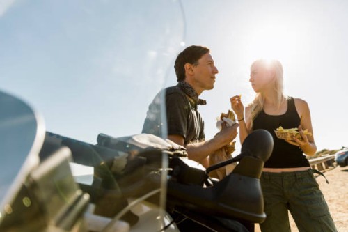 couple enjoying meal by motorcycle against sky on sunny day - junk food stock pictures, royalty-free photos & images