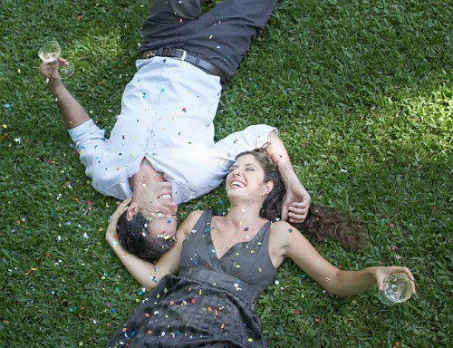 couple outdoors lying on grass with white wine and confetti laughing - garden decoration stock pictures, royalty-free photos & images