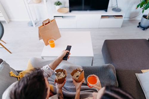 couple relaxing on sofa, watching television and eating takeaway food - junk food stock pictures, royalty-free photos & images