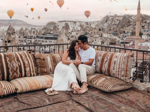 couple romantique en cappadoce assis sur un toit et regardant les montgolfières dans le ciel - travel photos et images de collection