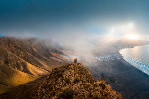couple standing on top of a cliff looking at sunset, lanzarote, spain - travel stock pictures, royalty-free photos & images