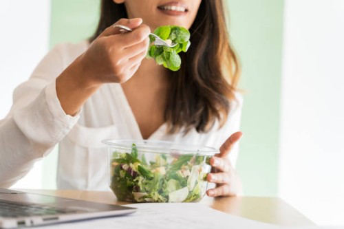 crop view of young architect eating mixed salad at desk - junk food stock pictures, royalty-free photos & images