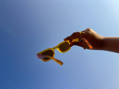 cropped hand holding sunglasses against blue sky background - fashion stock pictures, royalty-free photos & images