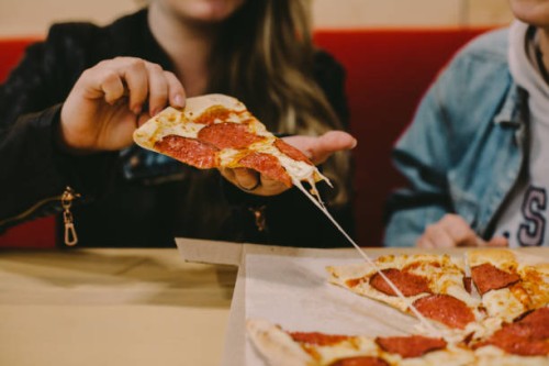cropped image of woman holding pizza slice at restaurant - junk food stock pictures, royalty-free photos & images