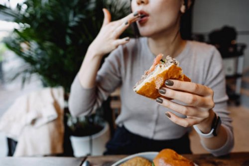 cropped shot, mid-section of young asian woman eating freshly made delicious cheeseburger in a cafe, licking her fingers. enjoying her lunch! people and food concept - junk food stock pictures, royalty-free photos & images
