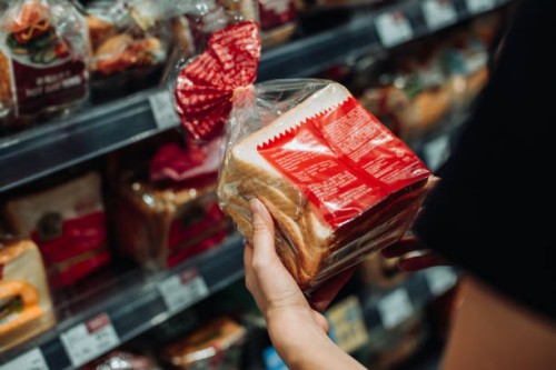 cropped shot of young asian woman grocery shopping in supermarket, shopping for fresh bakery and reading the nutrition label at the back of a packaged bread. routine shopping. healthy eating lifestyle - food photos et images 