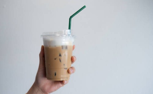 cropped shot view of someone hand holding a plastic cup of iced milk coffee against white wall. - junk food stock pictures, royalty-free photos & images