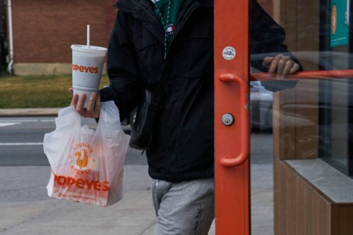 Customer with a takeout order exits a Popeyes fast food restaurant in the Queens borough of New York, US, on Sunday, Feb. 11, 2024. Restaurant Brands...