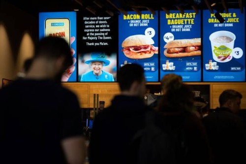 Customers queue beneath a tribute to tribute the late Queen Elizabeth II, at a fast food store inside King's Cross train station in London on...