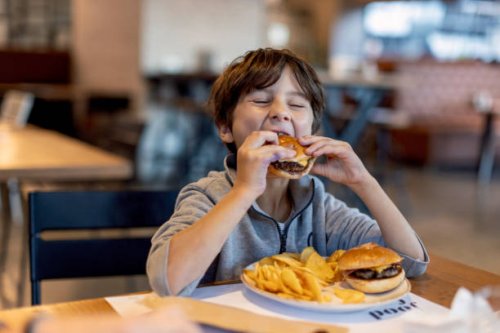 cute kid boy eats hamburger sitting in cafe. - junk food stock pictures, royalty-free photos & images