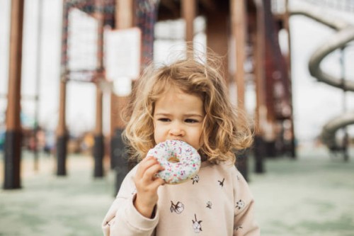 cute little girl biting sweet and tasty donut outdoors. unhealthy but delicious food - junk food stock pictures, royalty-free photos & images