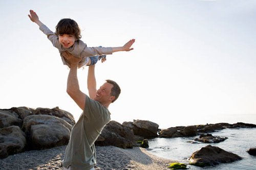 dad lifts young son above his head on beach - travel stock-fotos und bilder