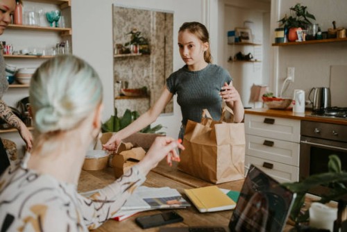 daughter holding container while looking at trans woman mother at home - junk food stock pictures, royalty-free photos & images