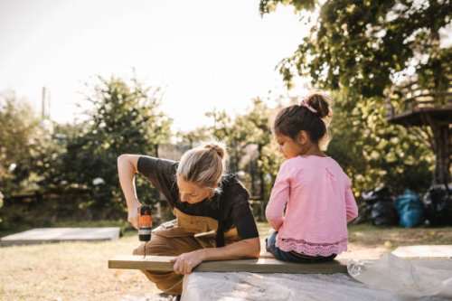 daughter looking at mother using drill machine on wooden plank in backyard - home decoration stock pictures, royalty-free photos & images