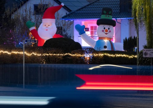 December 2022, Hessen, Frankfurt/Main: A giant illuminated Santa Claus and an equally large snowman stand in the front yard of a house decorated for...