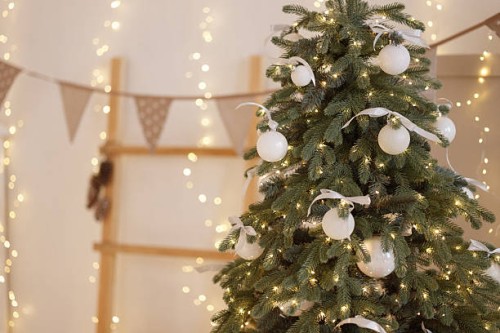 decorated christmas tree with white ornaments and lights in cozy room with white wall. - home decoration stock pictures, royalty-free photos & images