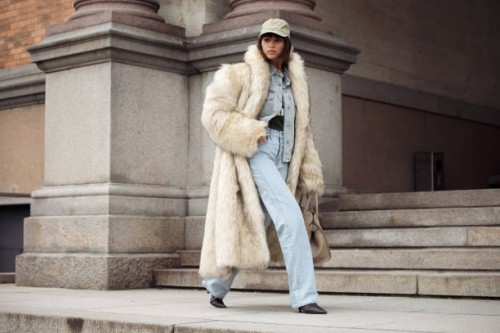 Deimante Kazenaite wears light blue jeans, matching denim shirt, light beige fur coat, beige bag and light pale green cap outside the MKDT fashion...
