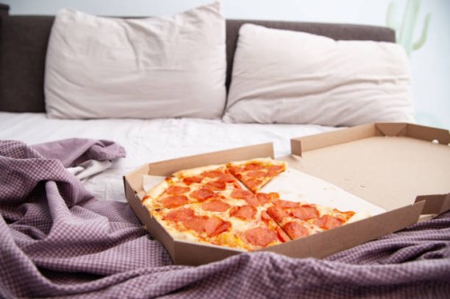 delicious delivered pizza in box on unmade bed in bedroom - junk food stock pictures, royalty-free photos & images