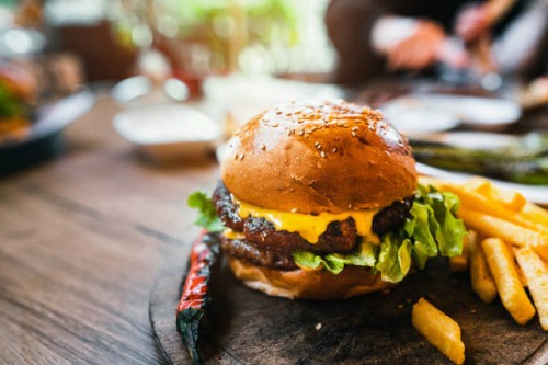 delicious double burger with french fries and vegetables on wooden cutting board - junk food stock pictures, royalty-free photos & images