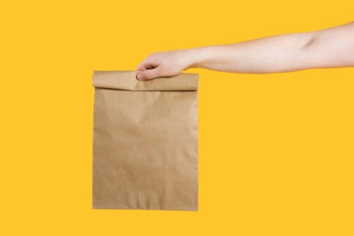 delivery service service concept. male hand holding eco craft takeout food bag on isolated yellow background studio. packaging mock up template. copy space - junk food stock pictures, royalty-free photos & images