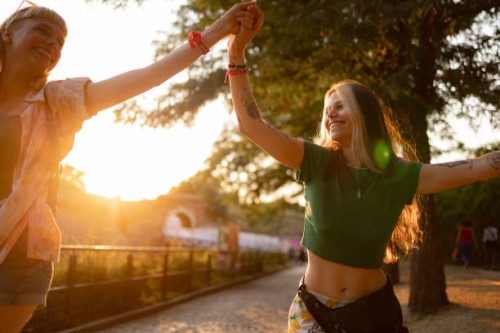 des femmes insouciantes se tenant la main lors d’un festival de musique au coucher du soleil. - concert photos et images de collection