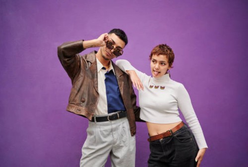 deux jeunes amis souriants prenant la pose devant un mur violet - fashion photos et images de collection