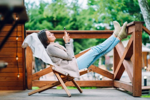 digital relaxation in glamping: brunette woman with feet up, surfing net and watching movies in phone, unwinds on log cabin patio - garden decoration stock pictures, royalty-free photos & images