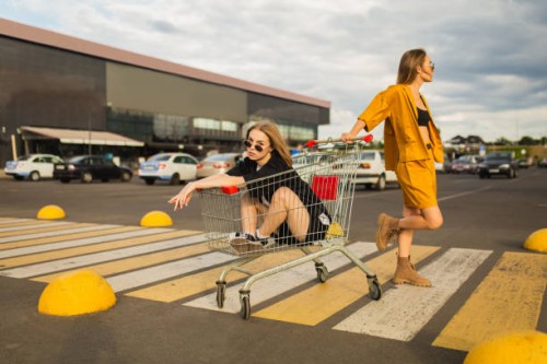 dos jóvenes rubias se divierten con el carrito de compras. mujer de moda - fashion fotografías e imágenes de stock
