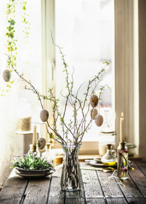 easter branches bunch with hanging easter eggs in glass vase on rustic wooden kitchen table with kitchen utensils, candle and decoration at window background - home decoration stock pictures, royalty-free photos & images