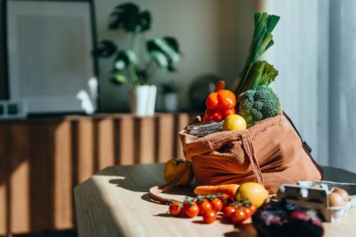 eco-friendly reusable shopping bag with multi-coloured fresh vegetables and groceries on the table at home. shopping with reusable grocery bag for plastic free and waste-free life. responsible shopping. zero waste and sustain