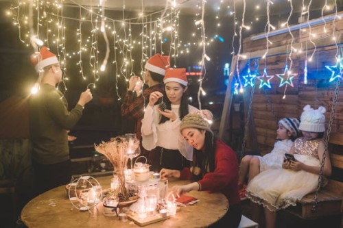 eine gruppe asiatischer chinesischer junger erwachsener, die sich auf ihr weihnachtsessen vorbereiten, zünden kerzen an und passen das weihnachtsliche lichterkettenlicht im vorgarten des hauses an. - garden decoration stock-f